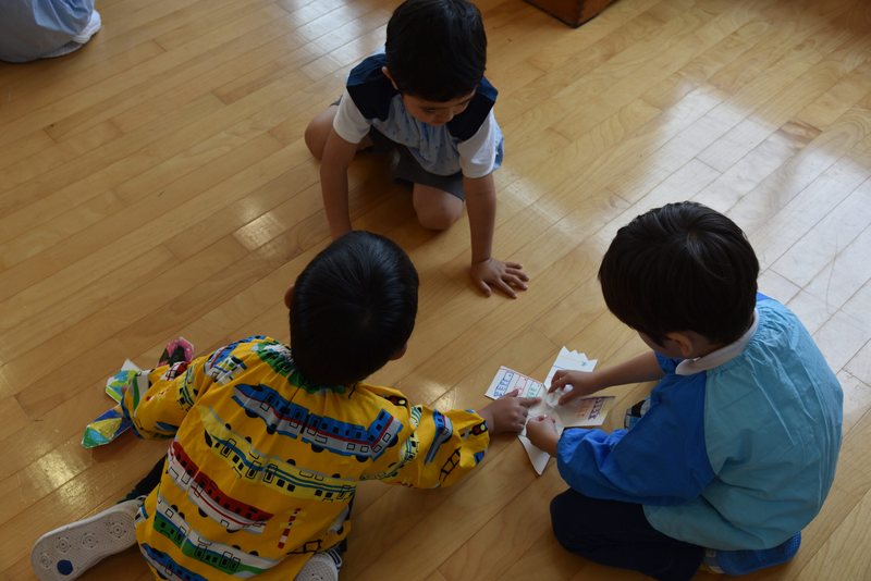 保育室の床で、友だちと一緒に製作あそびに取り組む園児たち